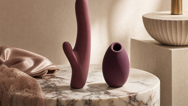 Due oggetti scultorei in silicone cipria e prugna a confronto su un piedistallo di marmo