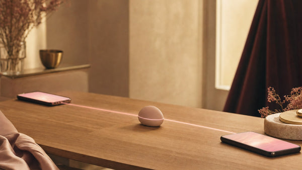 Due smartphone uniti da un filo di luce rosa che passa da un piccolo ovetto al centro del tavolo