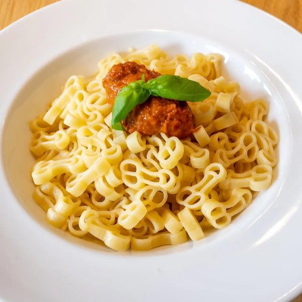Pasta a forma di pene servita con polpette e basilico su piatto bianco