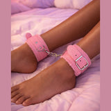 Cavigliere bondage rosa con orecchie in similpelle indossate su gambe sdraiate su letto rosa