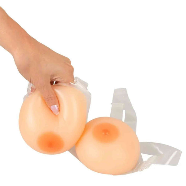 Protesi seno silicone colore pelle con capezzoli arancioni, tenute in mano su sfondo bianco
